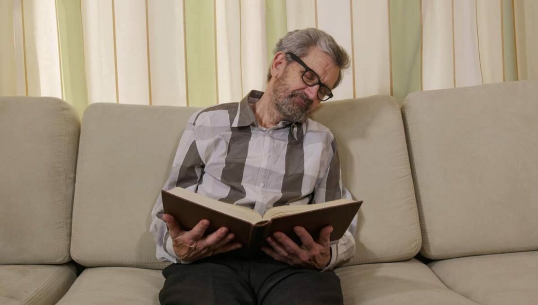 man falling asleep while reading sitting on the couch