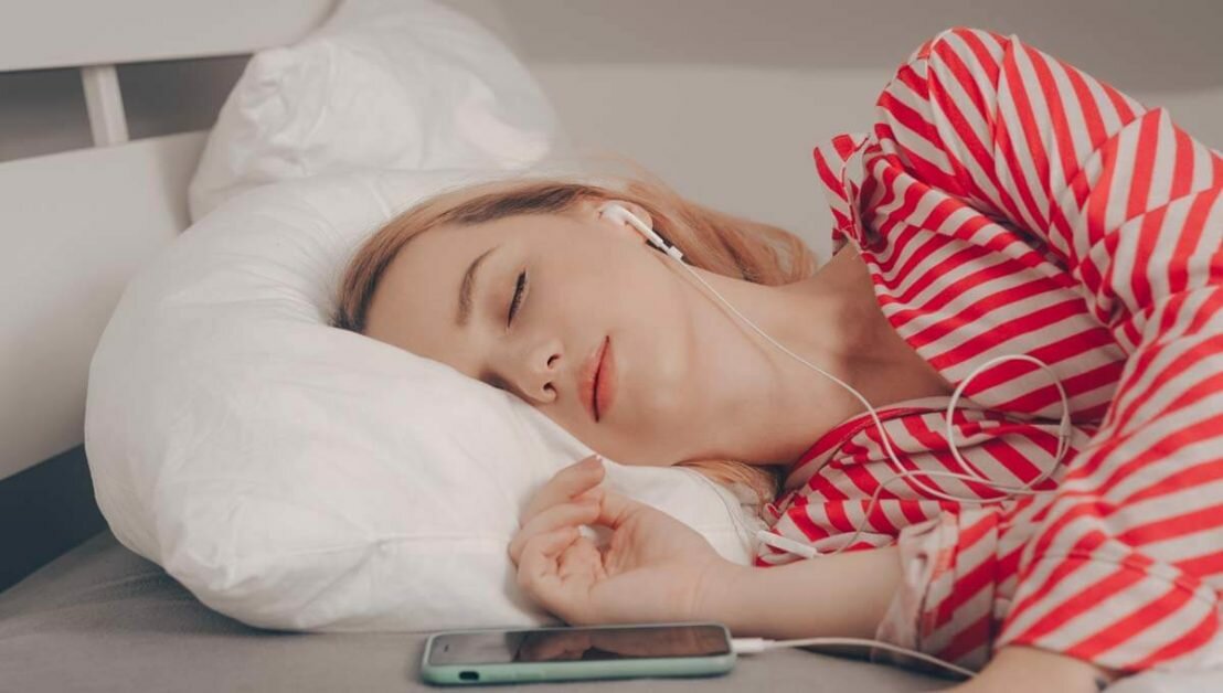 The girl sleep on the bed with music in the phone